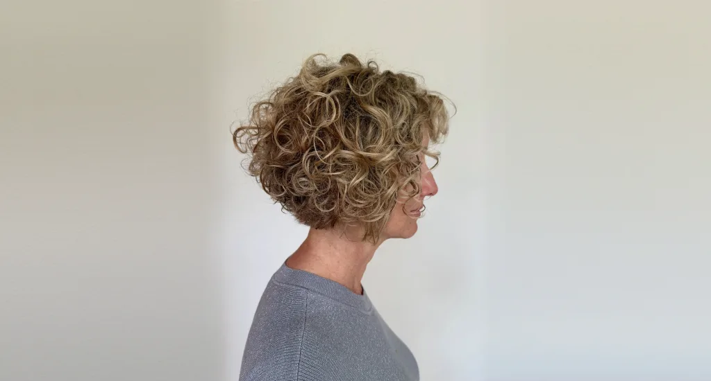 Side profile of a woman showcasing a voluminous, naturally curly blonde bob haircut with well-defined coiled layers.