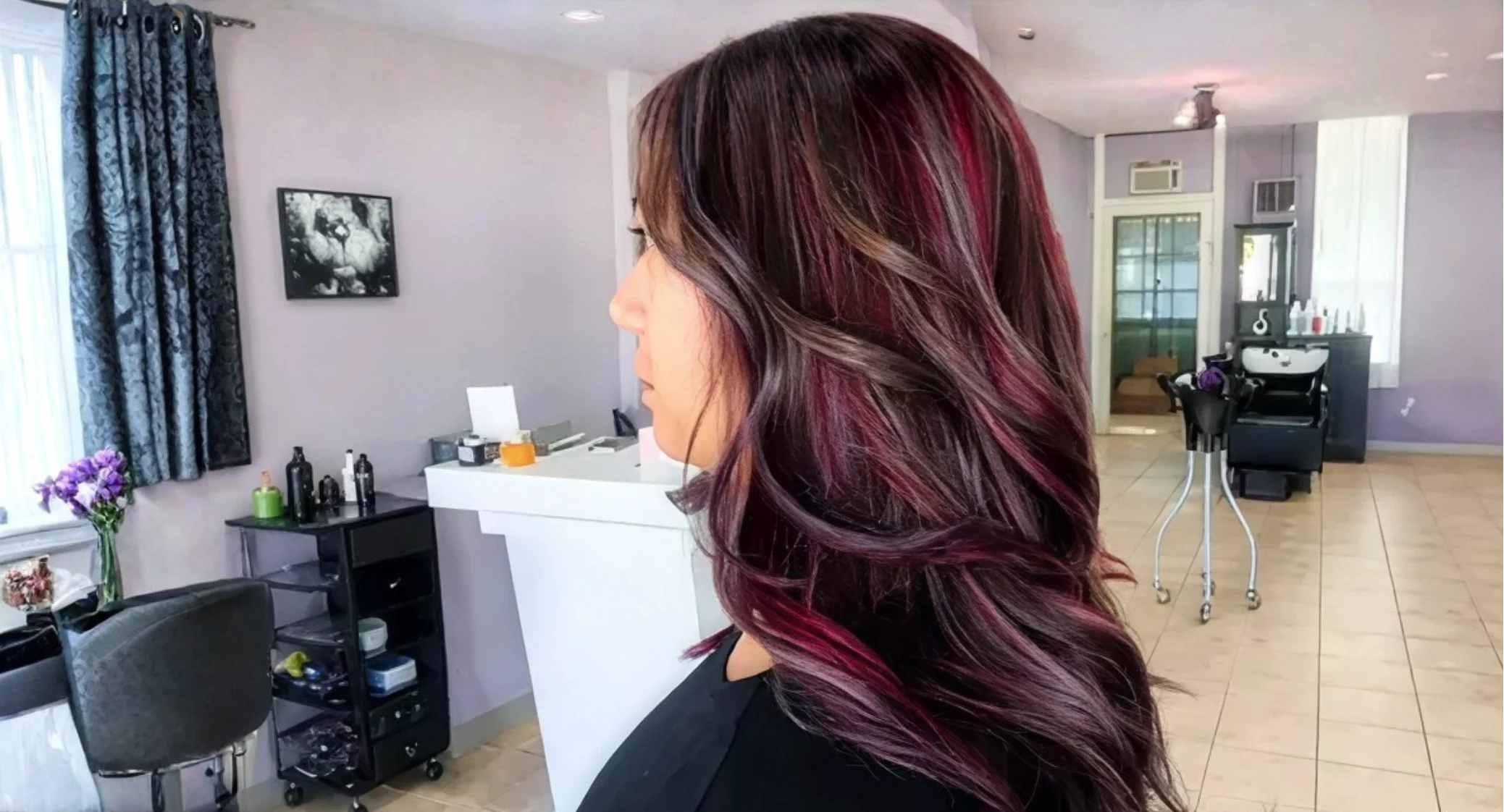 Side profile of a woman in a hair salon showing dark roots blending into deep purple and magenta ombre ends.