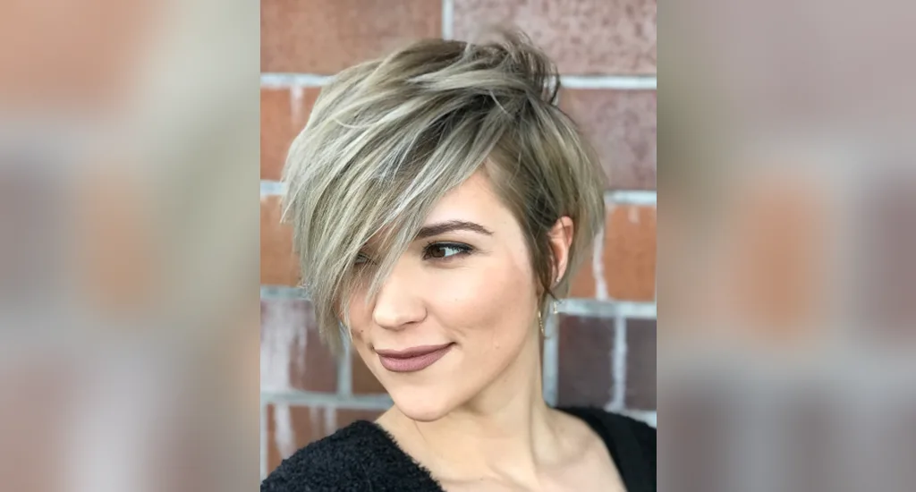 A woman wearing a textured blonde side-swept pixie cut with long side bangs.