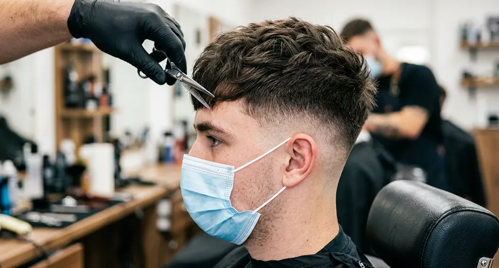 Close-up profile view of a young man with a short textured crop haircut and a seamless low skin fade.